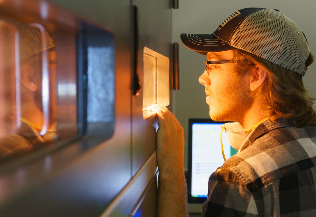 echnician inspecting SLS 3D printing machine during active build process for PA12 nylon parts